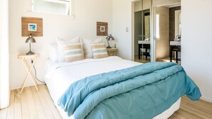 A bedroom with a bed, bedside tables, a window, and a bathroom visible through an open door.