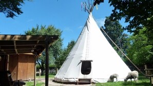 Ett vitt tipi-tält med en stege och en liten öppning, omgivet av en träkonstruktion och gräs.