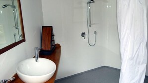 Ett badrum med ett vitt handfat, ett träfärgat tvättställ, en duschkabin med glasväggar och en vit duschdraperi.