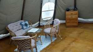 En ombonad inredning med en soffa, två fåtöljer i rotting, ett litet bord och ett träbord vid sängen med en lampa och en kopp.