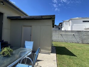 A patio area with a glass table and chairs, a small covered seating area, and a grassy yard.