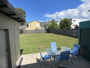 A backyard with a glass table and chairs, a small lawn, and a wooden fence.