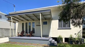 Een modern huis met een overdekte veranda, twee houten stoelen en een kleine tuin.