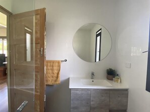 A bathroom with a glass shower door, a round mirror, a white sink, and a wooden cabinet.