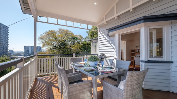 A balcony with wicker furniture, a glass table, and a potted plant. - Fantastic base for business meetings, dinner parties or family get together! (Toowong)