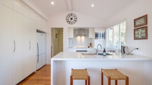 A modern kitchen with white cabinetry, a central island with stools, a clock on the wall, and framed pictures on the wall. - Fantastic base for business meetings, dinner parties or family get together! (Toowong)
