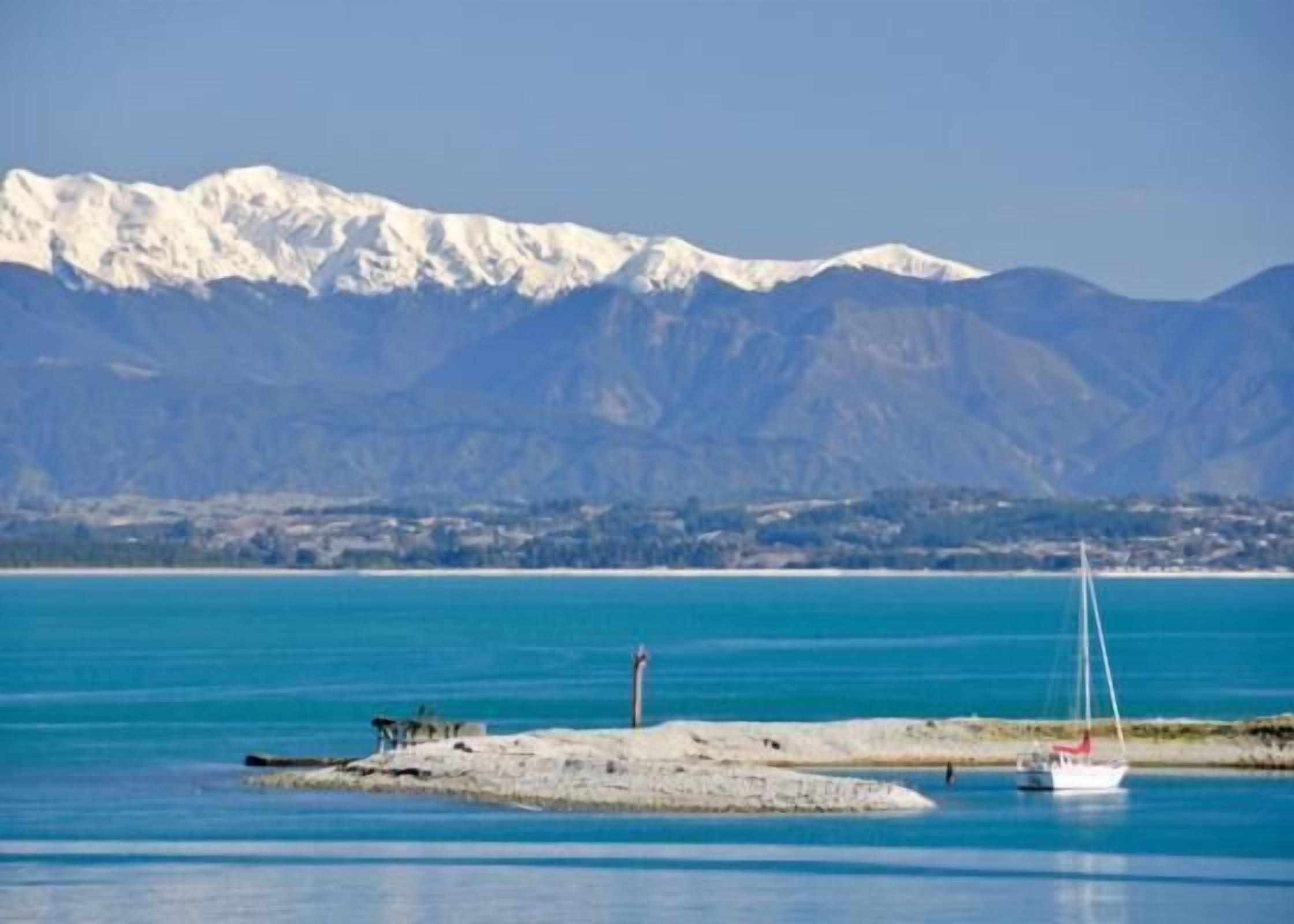 A coastal scene with a clear view of a mountain range in the background, a sandy beach, and a small boat anchored near the shore.