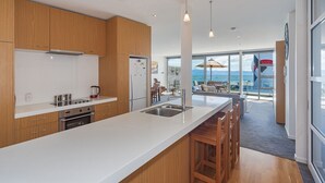 A modern kitchen with wooden cabinets, a large island, stainless steel appliances, and a view of the ocean through large windows.