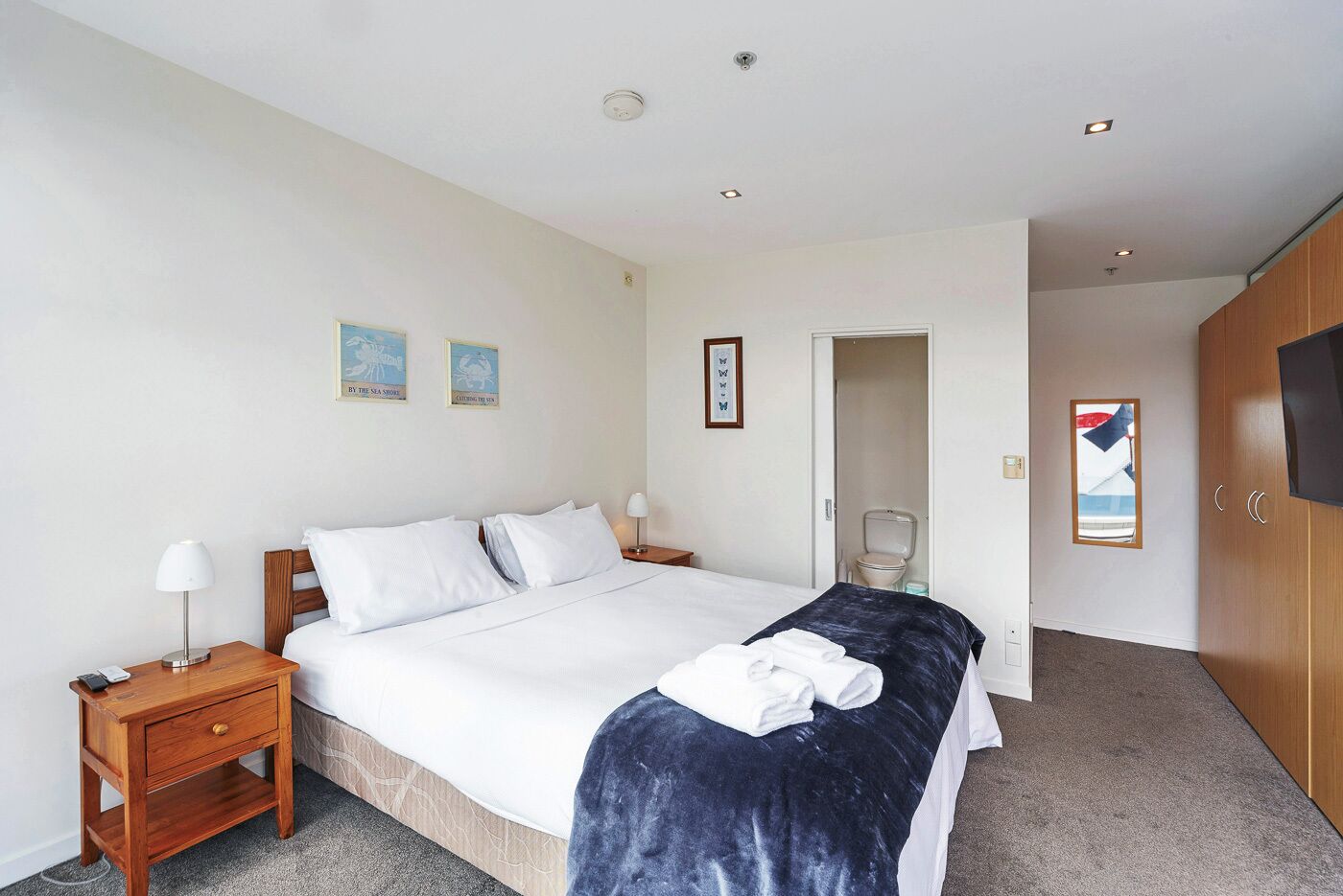 A hotel room with a bed, bedside tables, a TV, and a bathroom visible through an open door.