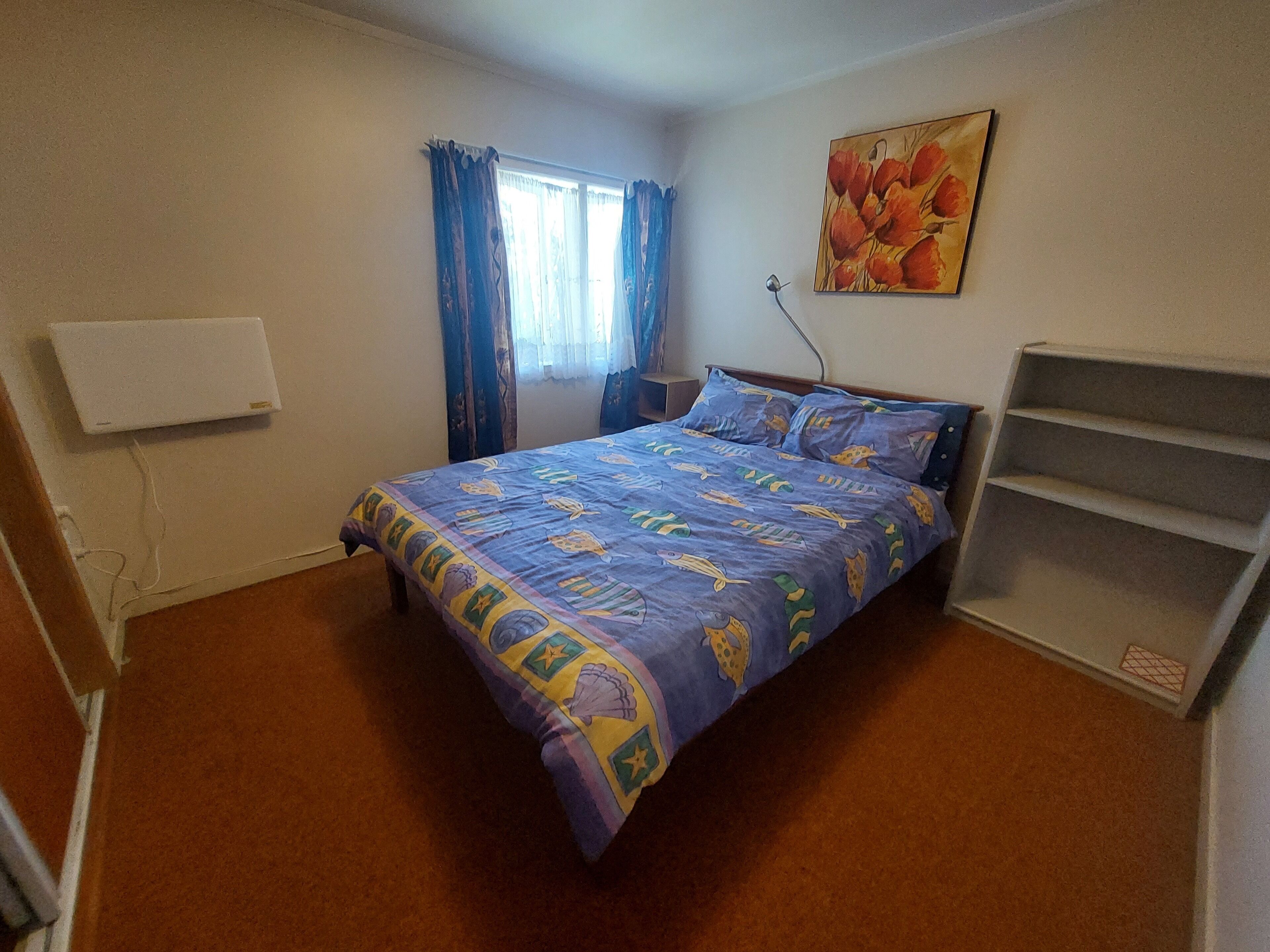 A bedroom with a bed, a nightstand, a wall-mounted lamp, a painting, and a built-in shelf.