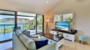 Amplia sala de estar con un gran ventanal corredizo que da a un balcón con vistas a la playa y las colinas.