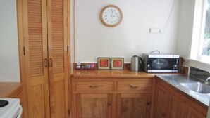 A compact kitchen with wooden cabinets, a microwave, a kettle, and a clock on the wall. - Te Mata Lodge - 2 Bedroom Cottage (Te Mata)