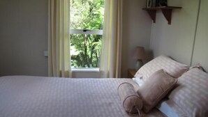 A neatly made bed with a patterned bedspread, a bedside lamp, and a window with curtains. - Te Mata Lodge - 2 Bedroom Cottage (Te Mata)