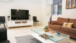 Ein modernes Wohnzimmer mit Flachbildfernseher, zwei schwarzen Stühlen, einem braunen Sofa und einem Glastisch mit Dekoration.