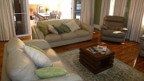 A living room with a sofa, armchair, and coffee table. There is a sliding glass door leading to a patio with outdoor furniture.