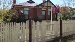 A two-story brick house with a white picket fence, a chimney, and a sign advertising executive cottages.