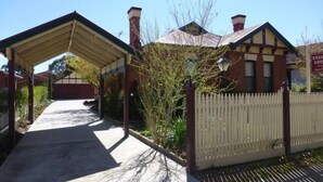 A covered walkway leading to a building with a brick facade and a white picket fence.