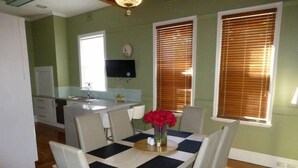 A dining area with a table set for four, a kitchen in the background, and a window with blinds.