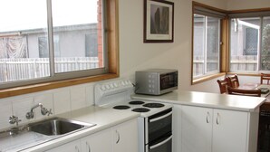 Eine kleine Küche mit Herd, Mikrowelle und Spüle. Schränke und ein Fenster sorgen für natürliches Licht.