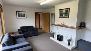 Ein Wohnzimmer mit einem grauen Ecksofa, einem Kamin aus weißen Ziegelsteinen und zwei gerahmten Bildern an der Wand.