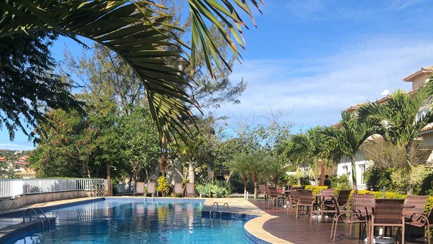 A swimming pool with a tiled edge, surrounded by lounge chairs and palm trees. - Wonderful house in Geribá, 4 suites, balcony and gourmet area. (BÚZIOS)