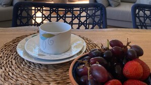 A table with a white cup and saucer, a bowl of grapes and strawberries, and a wicker placemat. - Wonderful house in Geribá, 4 suites, balcony and gourmet area. (BÚZIOS)
