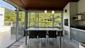 A modern kitchen with a large dining table and chairs, large windows with a view of greenery, and a wooden ceiling. - Ubatuba coverage for families - up to 12 people (including babies and children) (Ubatuba)
