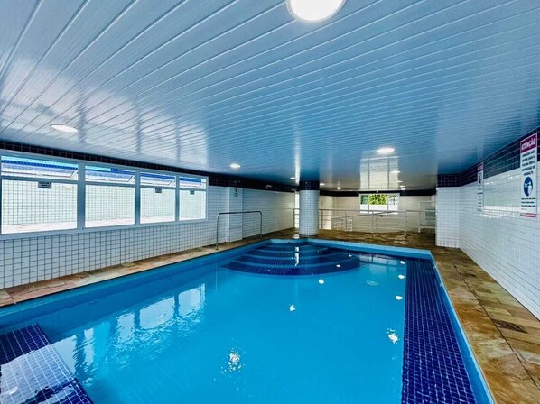 Piscina interior com paredes azulejadas e fundo azul.