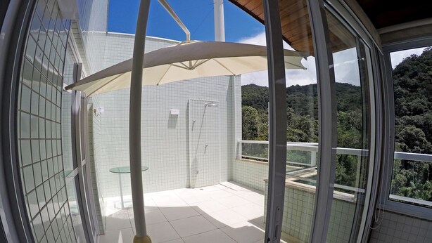 A modern bathroom with a glass shower enclosure, a small table, and a view of a lush green landscape. - Ubatuba coverage for families - up to 12 people (including babies and children) (Ubatuba)