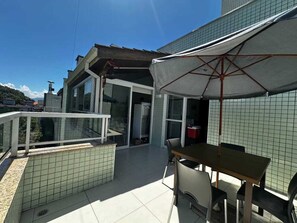 Varanda com mesa e cadeiras, corrimão branco e vista para a paisagem urbana.