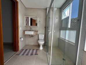 Ein modernes Badezimmer mit Duschkabine aus Glas, Toilette und Waschbecken mit Spiegel darüber.