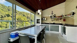 A modern kitchen with a large dining table, a view of lush greenery, and a rustic ceiling. - Ubatuba coverage for families - up to 12 people (including babies and children) (Ubatuba)