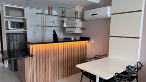 A modern kitchen with a wooden island, a dining area with chairs, and a microwave. - Loft with sea view. (apartamento 501 prainha Arraial do CABO)