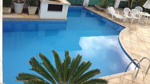A swimming pool with a small structure, potted plants, and white lounge chairs. - Loft with sea view. (apartamento 501 prainha Arraial do CABO)