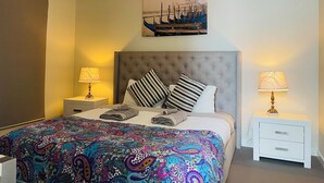 A bedroom with a large bed, two bedside tables, a headboard, and a painting of a cityscape. - Queen Lizzy Townhouses | 3BR, Parking, WiFi, Alfresco | City & Coast (Woodville South)
