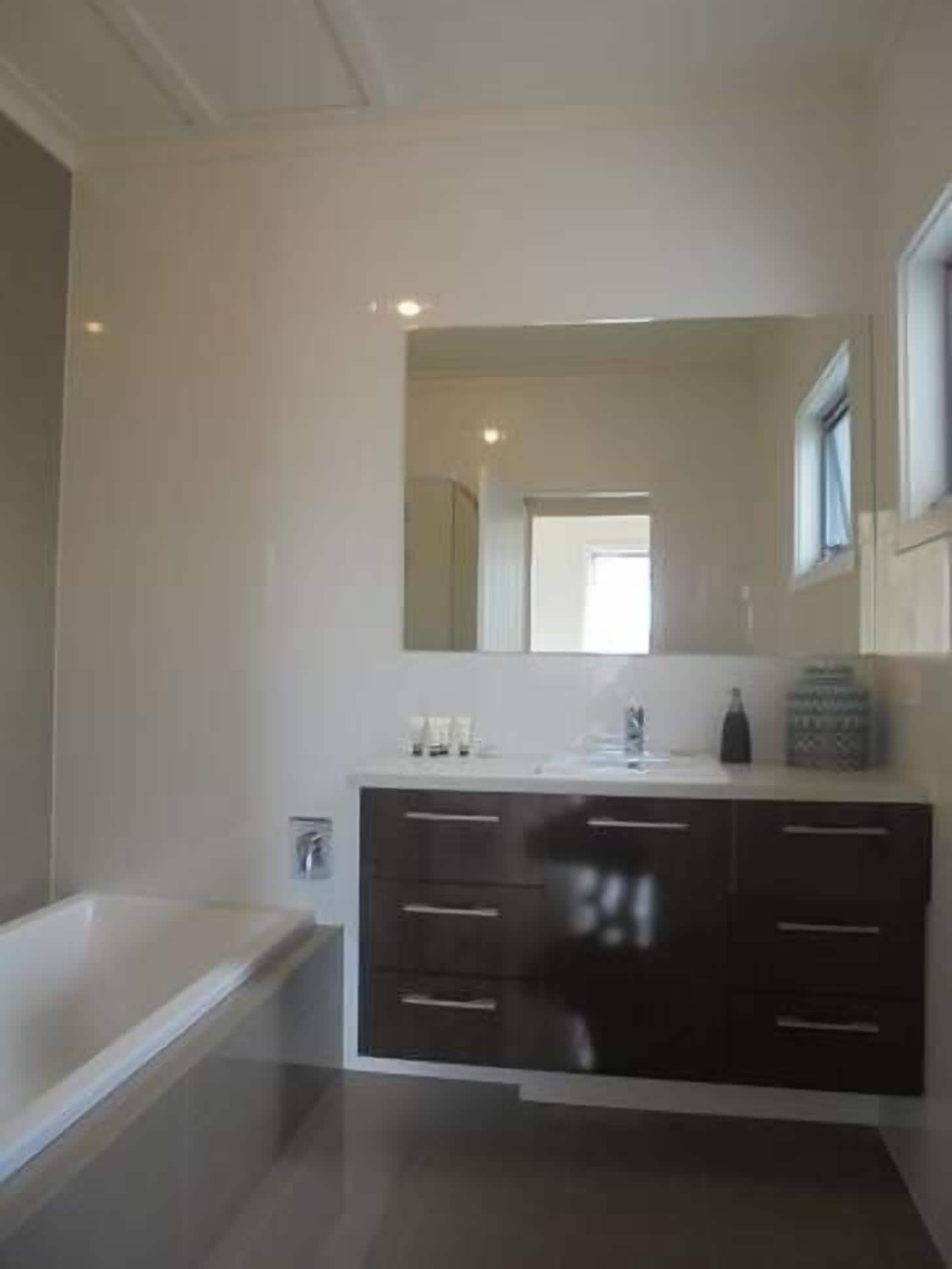 Un baño moderno con un espejo grande, muebles oscuros y una bañera.