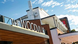 A hotel named "The Woodville Hotel" with a prominent sign, a brick facade, and a modern design. - Queen Lizzy Townhouses | 3BR, Parking, WiFi, Alfresco | City & Coast (Woodville South)