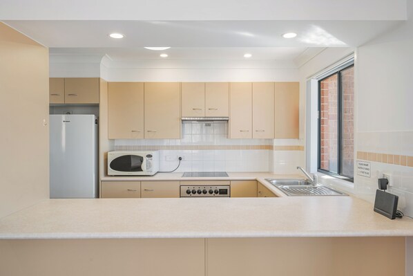 Una cucina compatta con mobili beige, un frigorifero bianco, un forno a microonde, una lavastoviglie e un lavello.