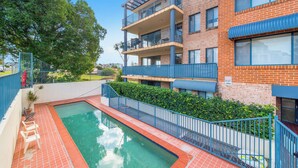 Un immeuble à plusieurs étages doté d’une piscine, de balcons et d’un panneau d’avertissement indiquant la présence d’une caméra de surveillance.