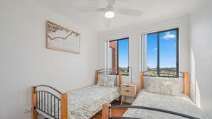Une chambre avec deux lits simples, un ventilateur de plafond, une fenêtre avec vue et une petite table de chevet.