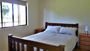 A bedroom with a wooden bed, a nightstand, a dresser, and a window with blinds.