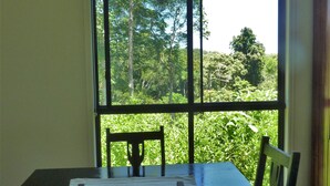 A dining area with a table and chairs, a window with a view of greenery, and a wooden floor.