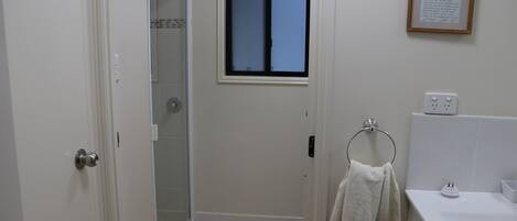 A bathroom with a shower, a window, a towel rack, and a framed note on the wall.