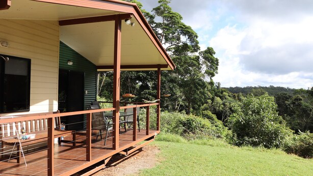 A wooden deck with outdoor furniture, a covered area, and a view of a forested landscape.