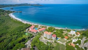 Luftaufnahme eines Küstenresorts mit Strandhäusern, einem Schwimmbad und üppiger Vegetation.