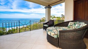Ein Balkon mit Korbmöbeln und Blick auf einen Strand.