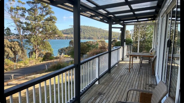 Una terraza de madera con barandilla de vidrio que da a un lago y colinas.