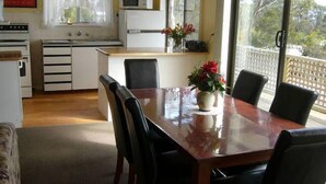 Una cocina compacta con electrodomésticos blancos, una mesa de comedor con sillas y vistas al exterior a través de amplias ventanas.