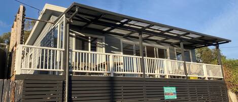 A beach house with a covered balcony, a wooden fence, and a sign indicating the property name.