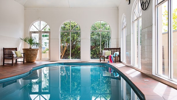 A pool area with a clear view of the outdoors through large arched windows, a bench, and a potted plant. - Courthouse Merindah - Villa in Town Centre (DAYLESFORD)